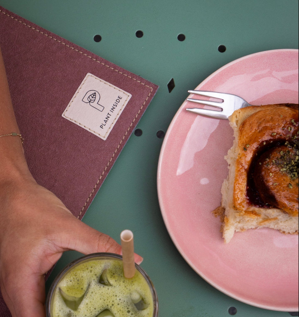 Close-up of Plant Inside logo stitched on a vegan MacBook case, with a hand holding a green drink and a slice of cake – everyday slow living and sustainable design