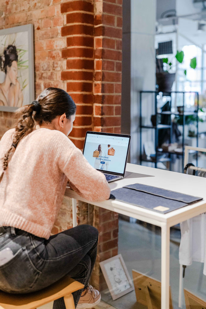 A young woman working on her laptop in a coworking space, with Plant Inside’s navy blue vegan laptop case placed beside her – a quiet statement of conscious style