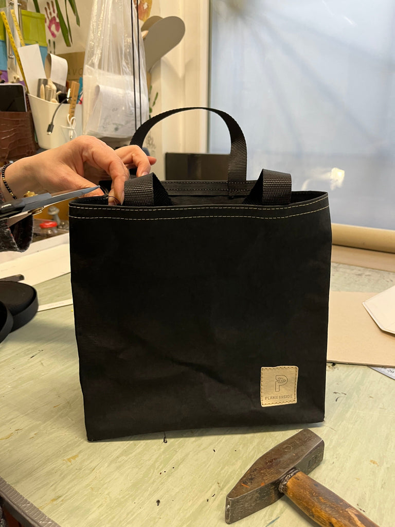 Close-up of Plant Inside vegan Lunch Bag being handcrafted in a Polish workshop, showing artisan’s hands with scissors, sewing tools and the stitched logo in focus – sustainable local production