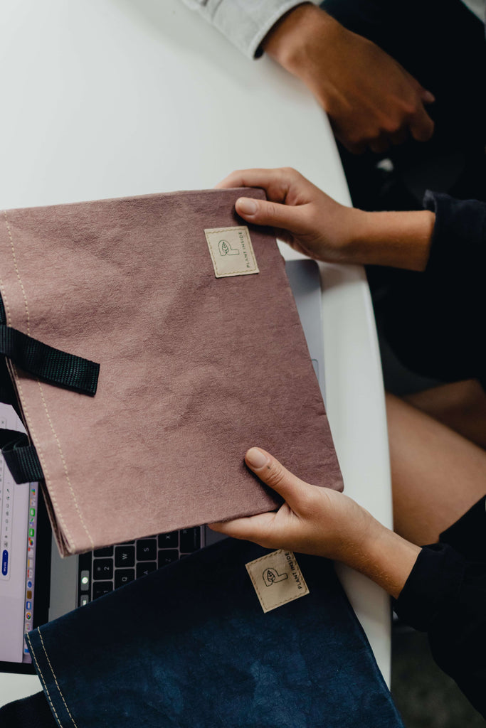 Woman holding a vegan Plant Inside lunch bag in pastel plum over a white table with a laptop and another lunch bag – symbol of thoughtful gifting and modern, conscious design