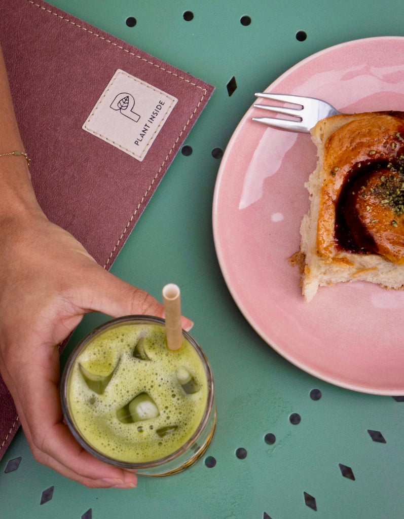 Vegan Plant Inside MacBook case in pastel plum on a green table – hand holding a cup of matcha and a pink plate with cake, symbol of calm winter rituals and conscious design