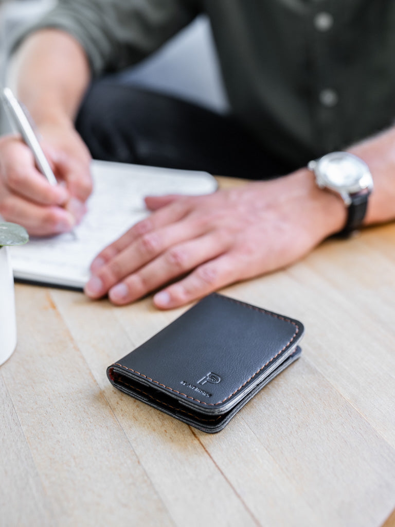 Close-up of a vegan Plant Inside wallet on a café table – blurred hands in the background writing in a notebook. Symbol of mindful living and timeless design