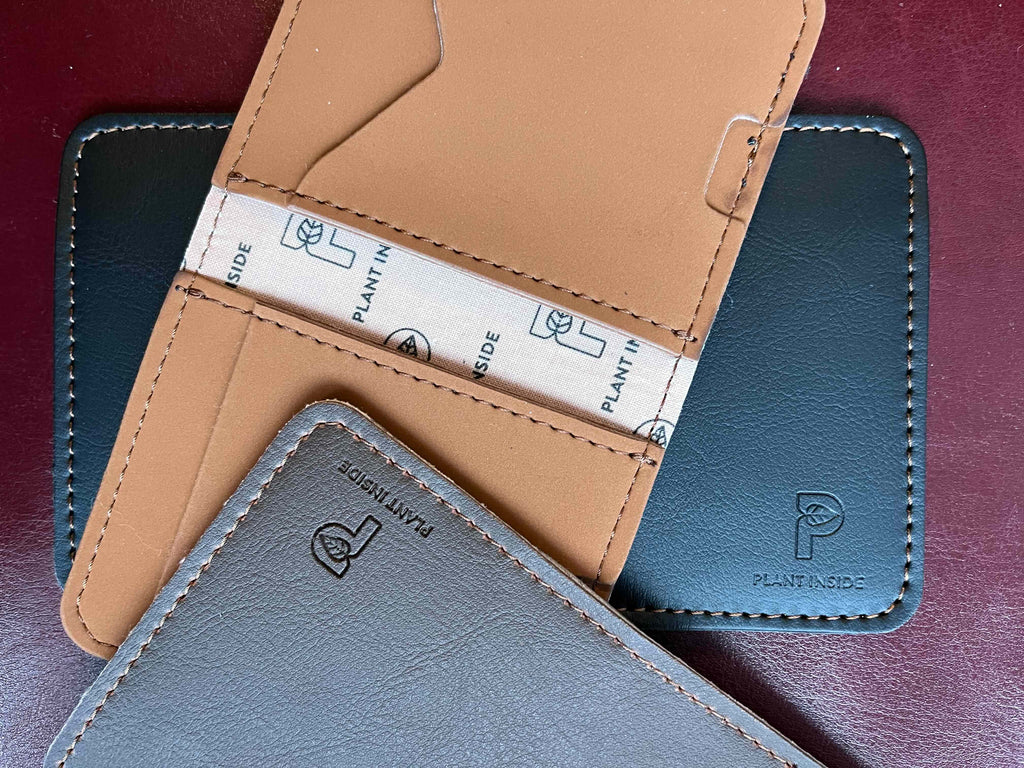 Three Plant Inside vegan wallets in black, camel and brown, layered on burgundy Viridis® leather – showing logo details, organic lining and elegant plant-based design