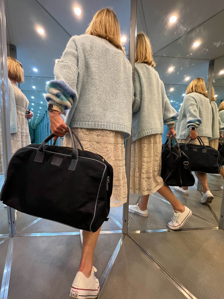 A woman seen from behind holding a sustainable Plant Inside weekend bag in a mirrored room, with reflections highlighting its minimalist and eco-conscious design